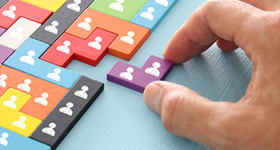 hand placing a purple puzzle piece into a colorful puzzle illustrating teamwork and connection with seven puzzle pieces visible