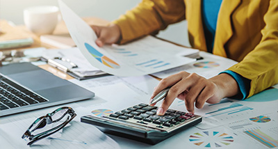 person calculating financial data with a calculator surrounded by charts and graphs on a desk using a laptop and holding documents related to budget planning and analysis 4 financial management strategies